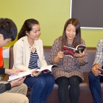 Four students are sitting on a couch reviewing the book club book.