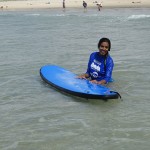 Tharshika stands in the shallows with her surf board