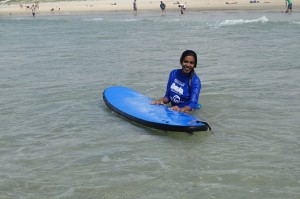 Tharshika stands in the shallows with her surf board