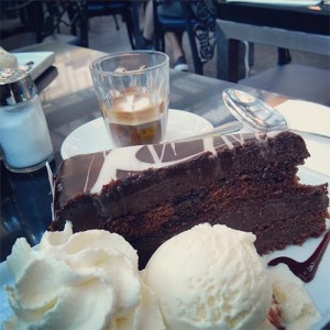A piece of chocolate cake sits next to a Macchiato for size comparison.