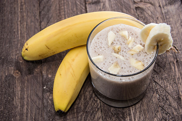 banana smoothie in a short glass accompanied by 2 bananas