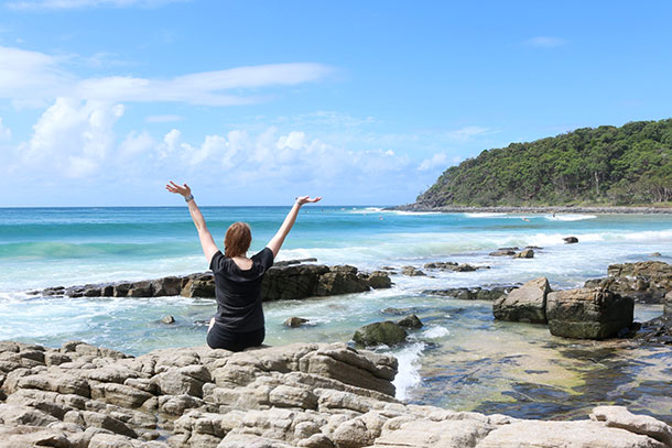 Student facing the ocean at Noosa with hands held up in the air