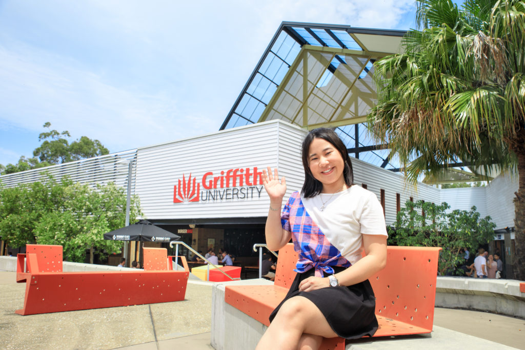 And sitting on a bench waving with griffith logo in the background