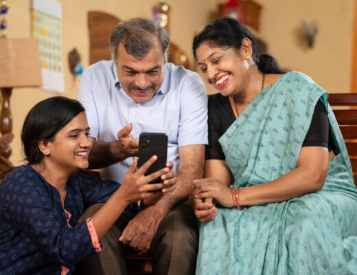 Indian teenager daughter showing Mobile phone app to middle aged parents at home - concept of social media sharing, Internet or technology and family bonding